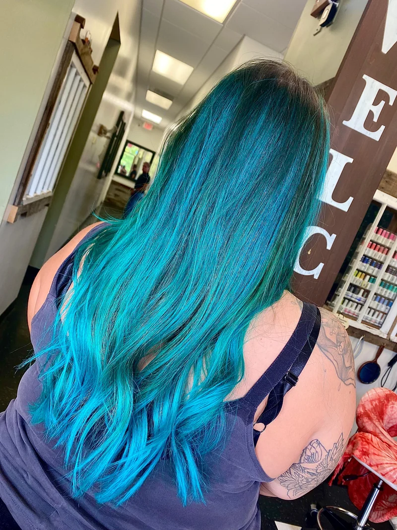 Long teal-blue hair with darker roots and soft movement.