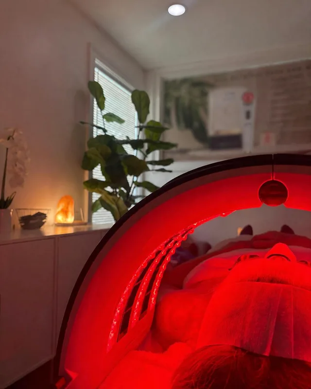 A client relaxing beneath red LED light in the warm Good Vibes facial room